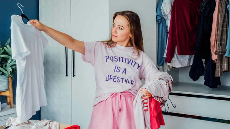 A woman considering clothes as she cleans out her closet.