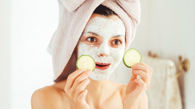 Woman with mask holding cucumber slices