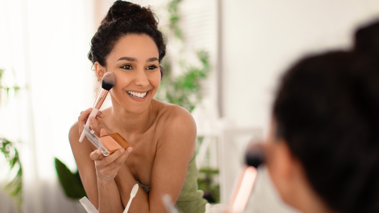 woman applying bronzer in mirror