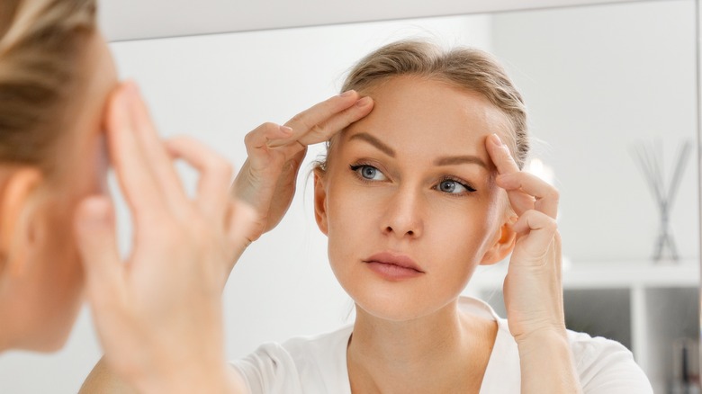 woman examining face in mirror