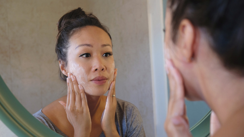 woman exfoliating face in mirror