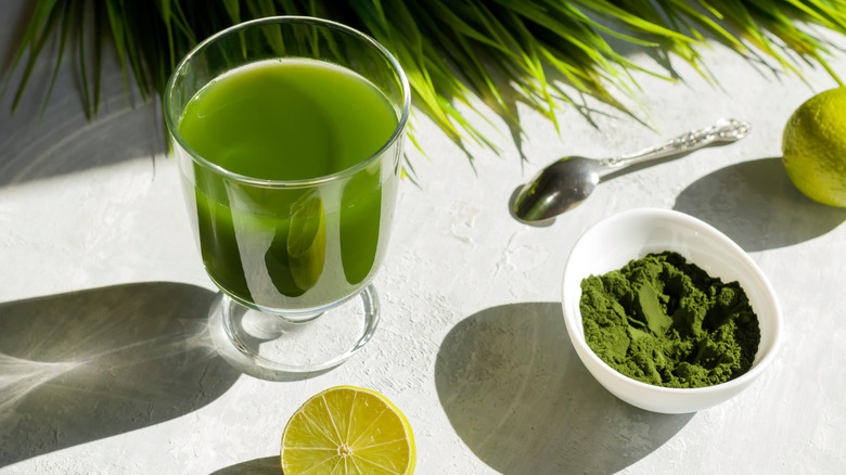 Glass of liquid chlorophyll next to greens and powdered supplement