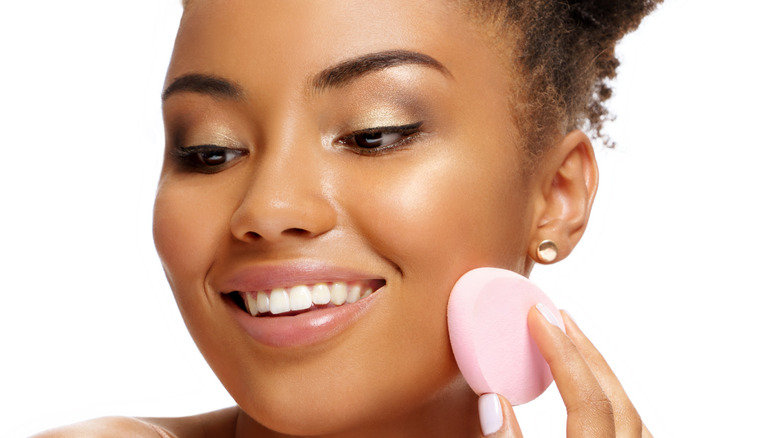 smiling woman holding makeup sponge to face