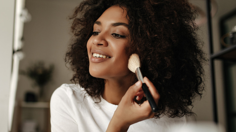 woman applying makeup on cheeks with brush