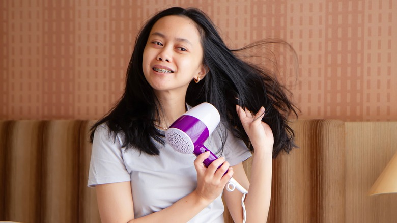 Woman sitting on bed blowdrying hair