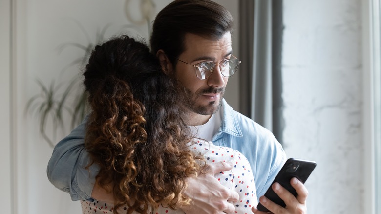 man looking at phone hugging woman