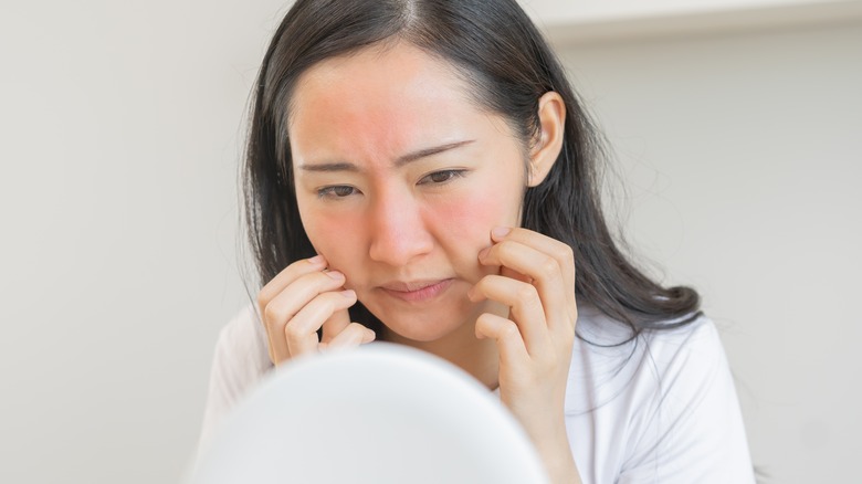 Woman examining rash on face