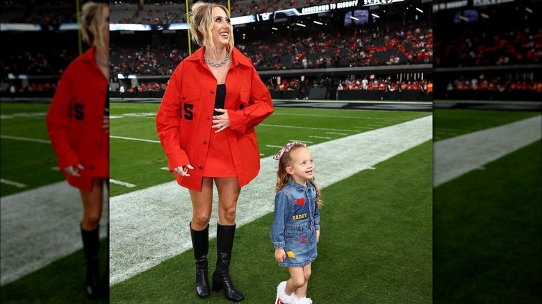 Brittany Mahomes posing by the pitch with her daughter.