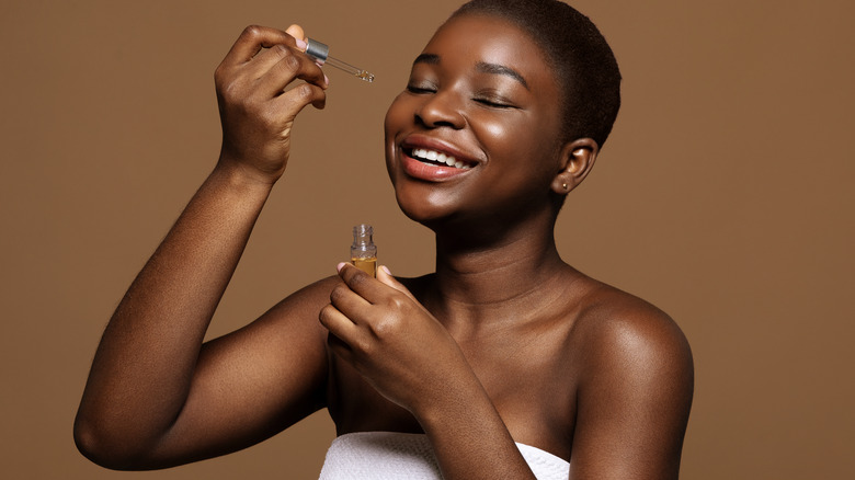 Smiling Black woman applying face oil