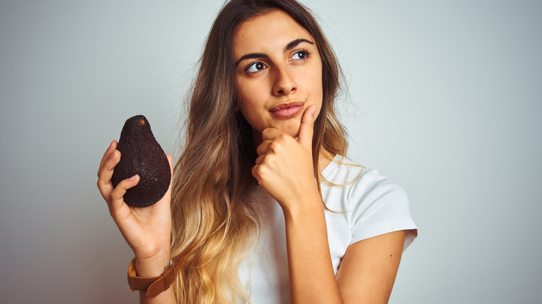 Blonde woman holding avocado thinking