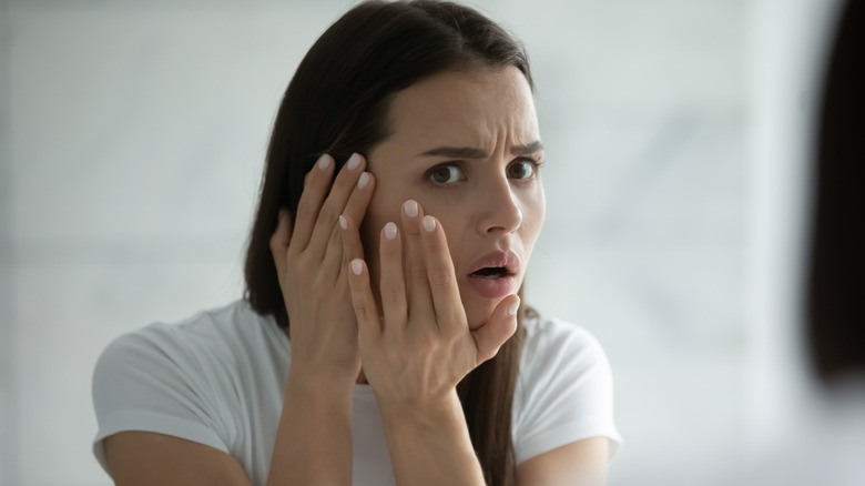 woman looking at skin in mirror with concern