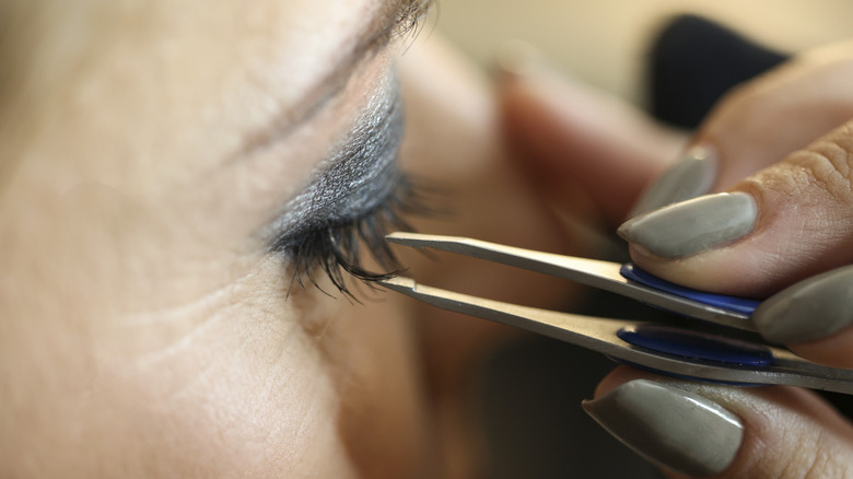 woman using tweezer on eyelashes