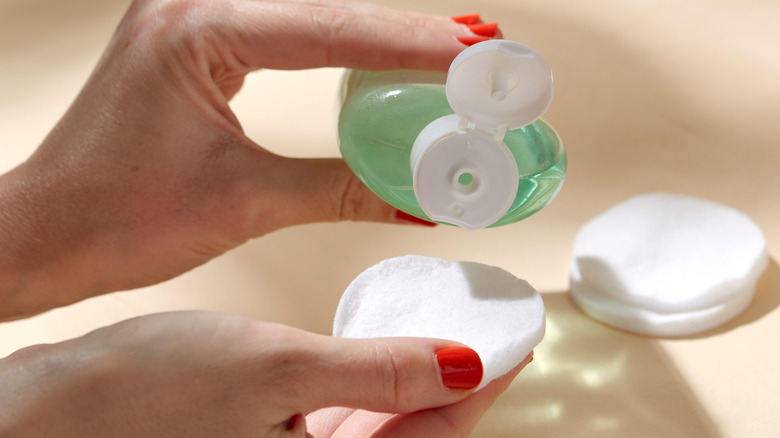 female hands pouring a serum/toner onto a cotton pad