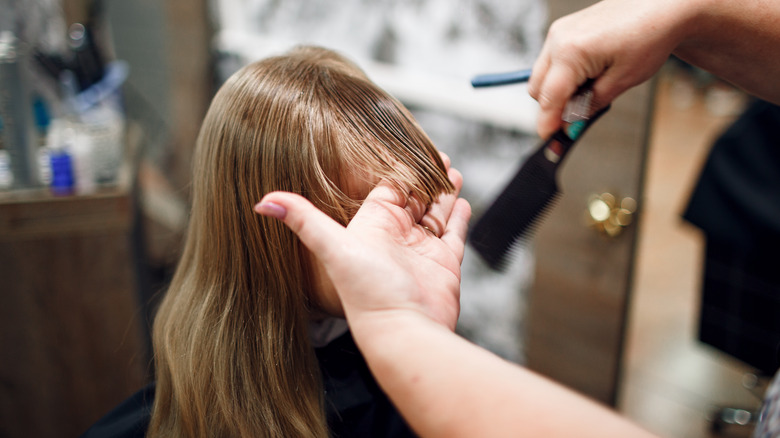Hairstylist cutting girl's bangs