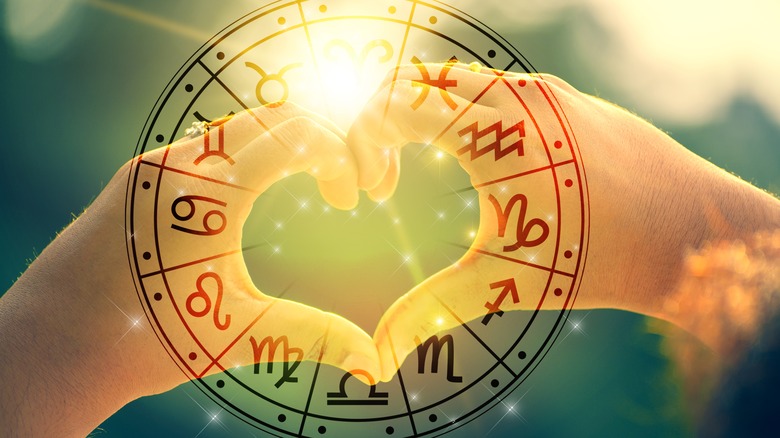 Zodiac signs pictured against two hands forming a heart