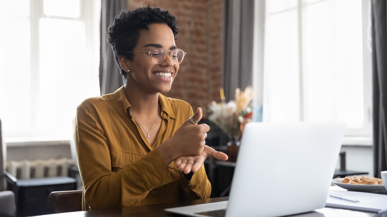 Woman smiling at her desk with laptop, breakfast, and notes