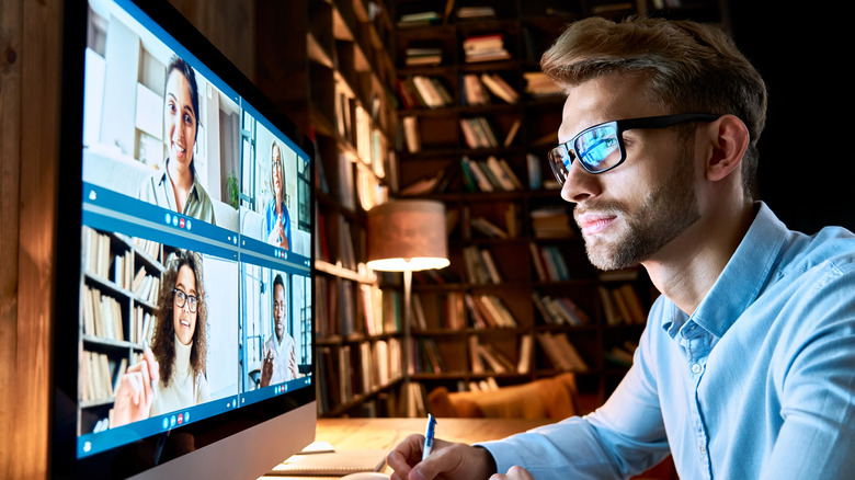 Man writing at desk while engaging in video call with colleagues