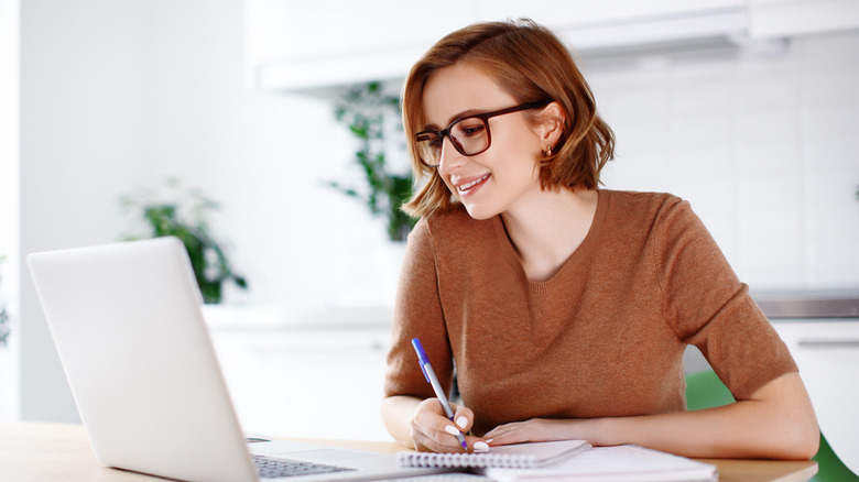 Woman writing in notepad with open laptop on desk