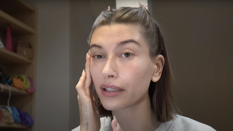 Hailey Bieber applies peptide serum to her face before doing her makeup in a video tutorial.