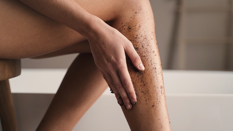 Woman applying coffee scrub to leg