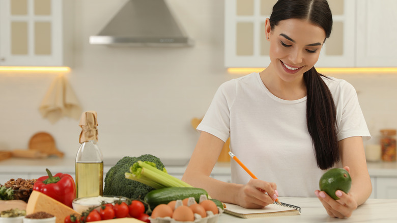 woman writing in her notebook while holding food