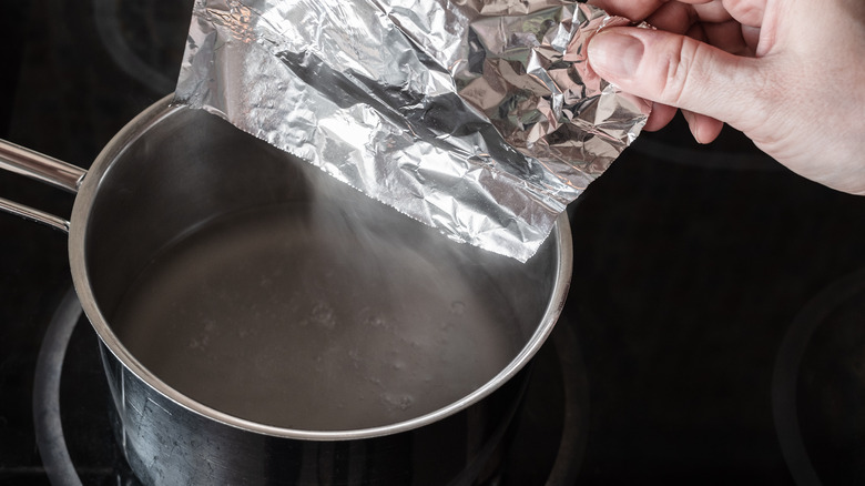 Person lining a pot with aluminum foil