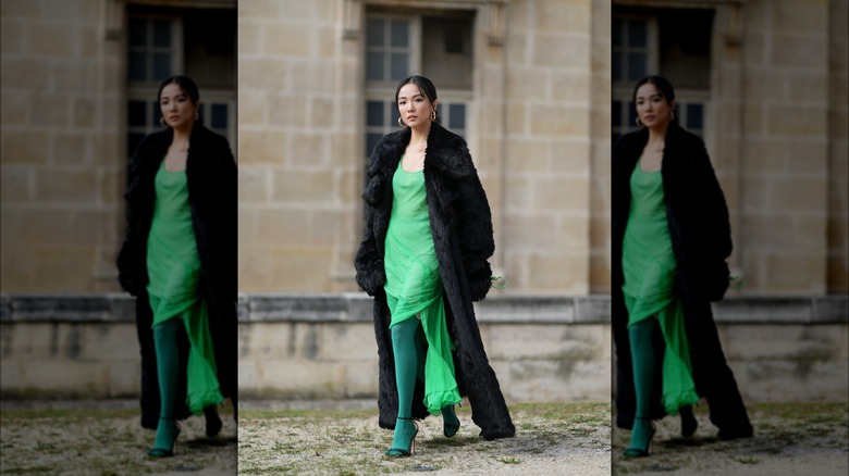 Woman wearing green tights, green dress, black maxi coat