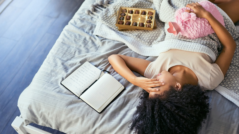 Woman in bed with hot water bottle, journal, and chocolate