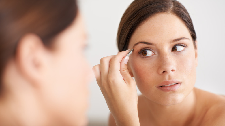 A woman tweezing her eyebrows