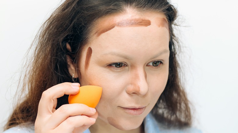 Woman applying dark bronzer to face with a sponge