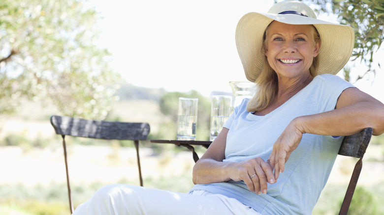 Woman sits in patio chair wearing sun hat