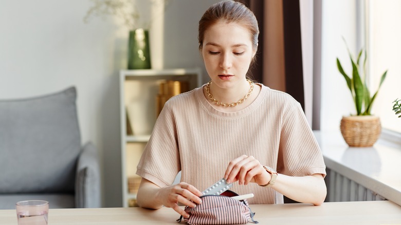 Woman putting oral conrtaceptive in cosmetic bag