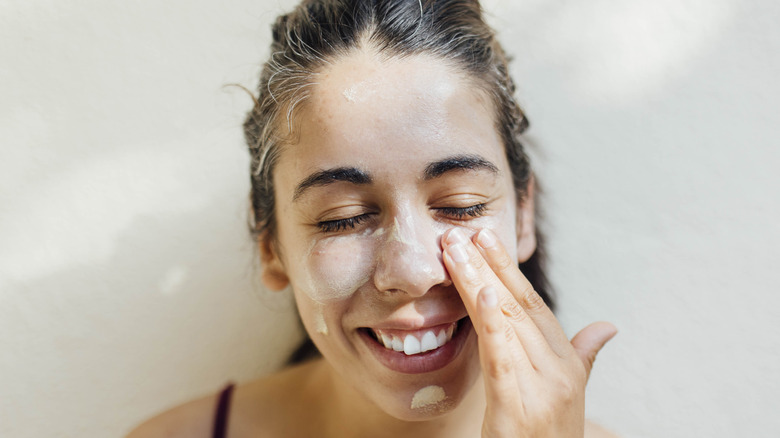 Smiling woman applying sunscreen on face