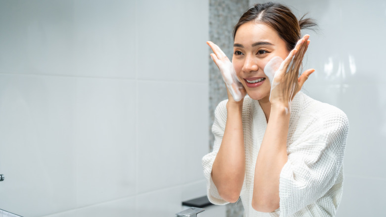 Woman in white bathrobe washing her face