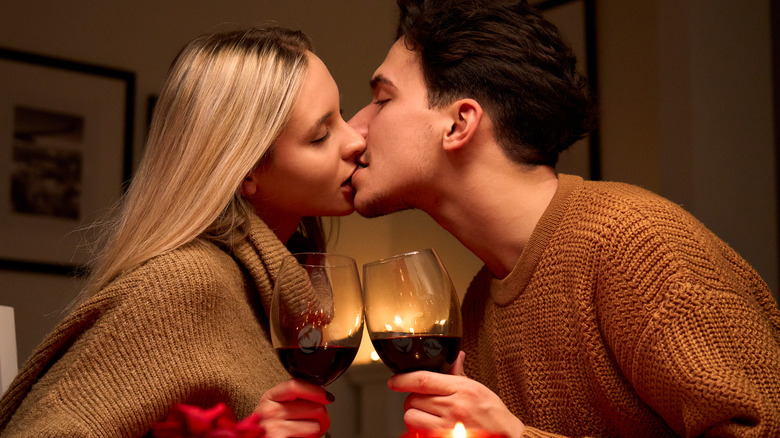 Couple kissing while holding wine glasses