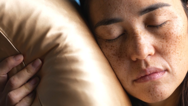 Freckled woman hugging silky pillow