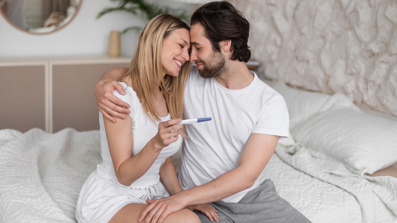couple embracing, holding positive pregnancy test