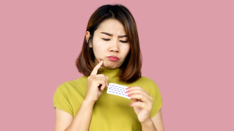 Model looking at pack of oral contraceptives with thinking expression