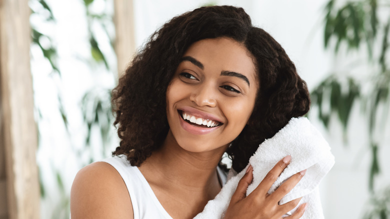 Woman drying hair with white towel while smiling