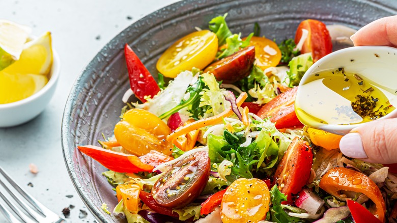 Person pouring olive oil on salad