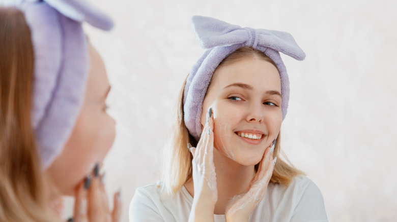 teen girl washing her face in the mirror