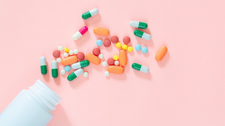 Medication bottle spilling pills on pink background