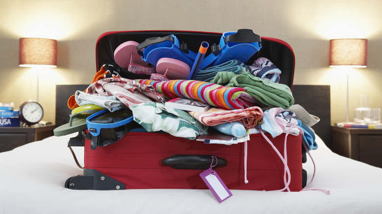 Overflowing suitcase sitting on hotel bed