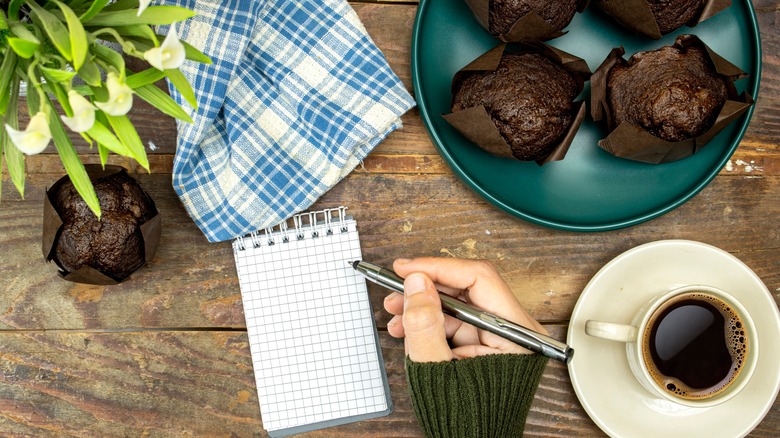 person writing near muffin plate