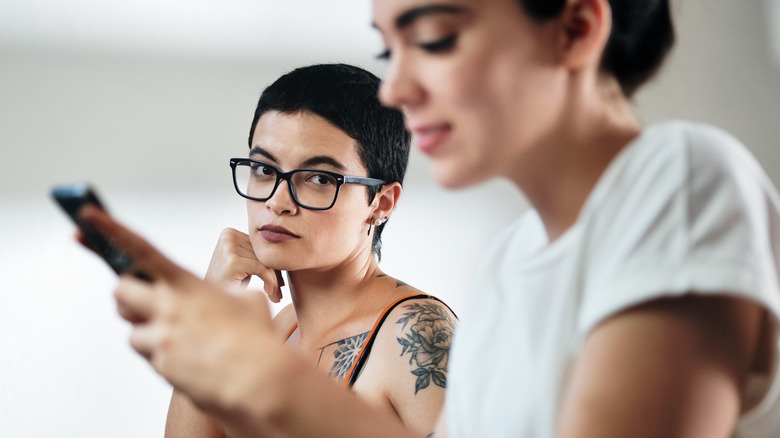 Jealous woman watching her partner smile at phone