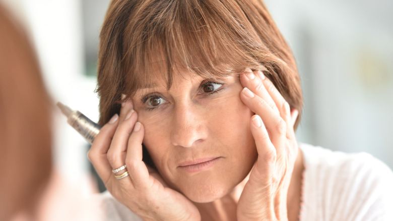 Woman looking in the mirror holding concealer