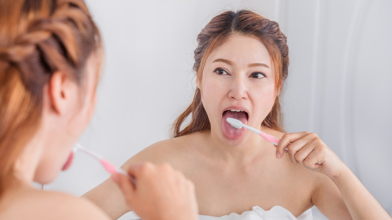 woman brushing tongue in mirror
