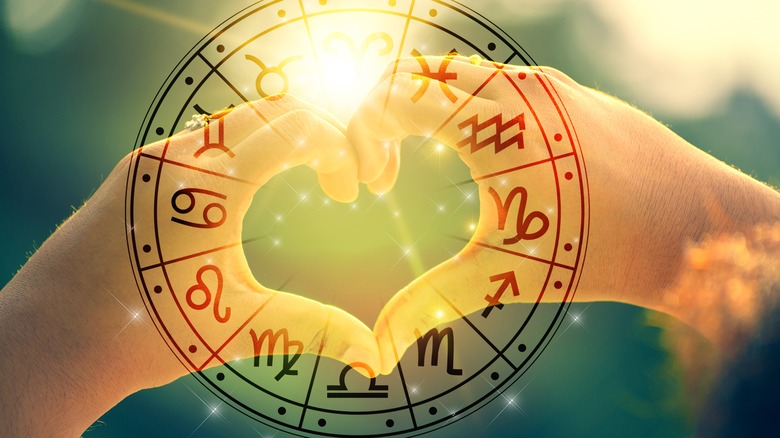 Two hands making a heart shape behind a zodiac calendar