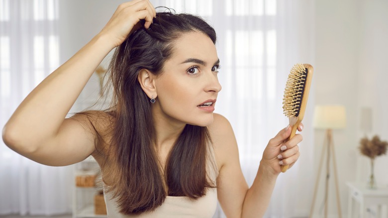 A woman brushing her hair and looking at her scalp