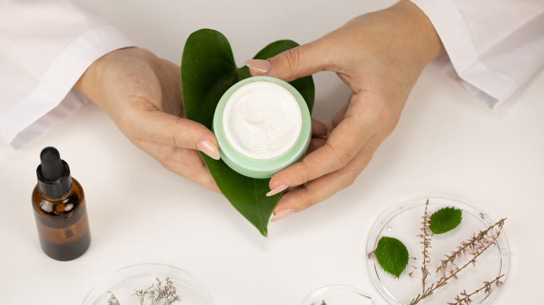 Woman holding a heart-shaped leaf with moisturizer placed on top